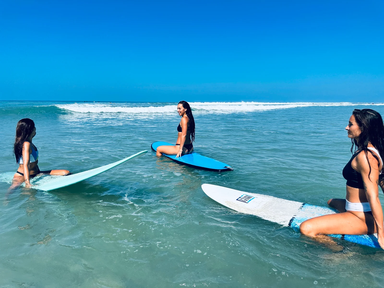 Three surfers sitting on their boards in the ocean at Playa Guiones, from NSI’s Spanish and Surf program.
