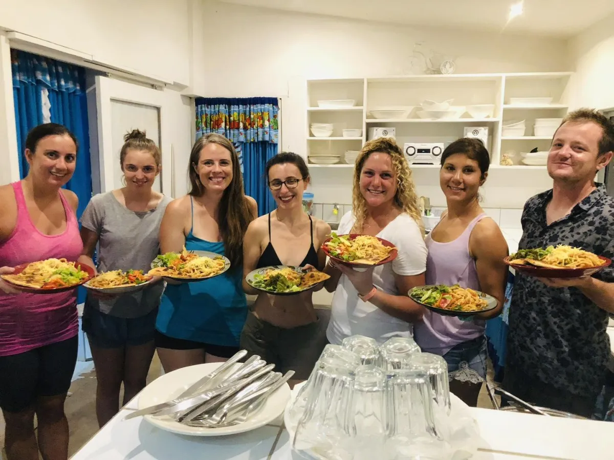 Seven people holding plates of food in a dining area, from NSI’s homestay imagery.