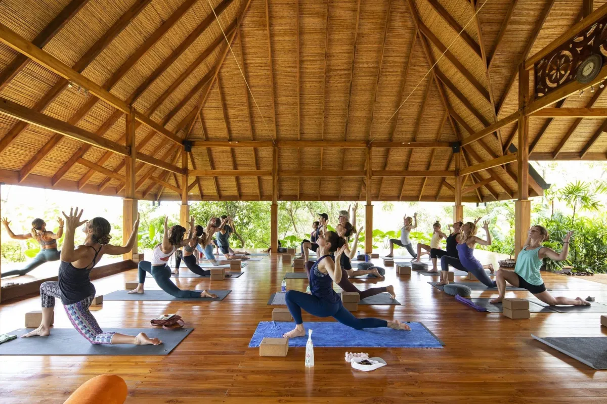 A group practicing yoga on mats beneath an open-sided timber roof.